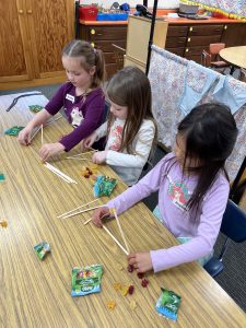 Kindergarten students from Belleview Elementary, Amelia, Opal, and Journey, build structures from popsicle sticks and gummy bears. Guest engineer Andrew Batalya, Delve Underground Engineering