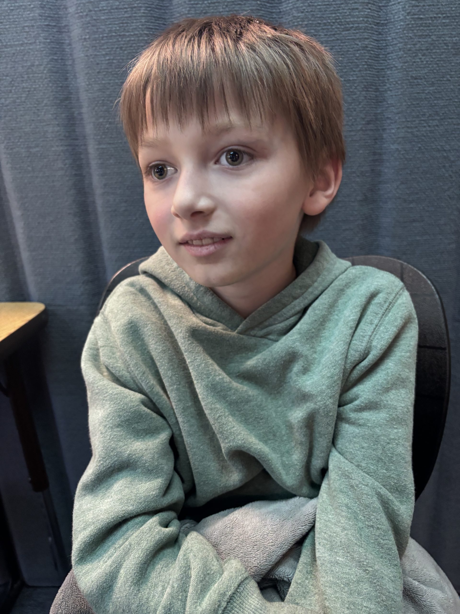 Jameson smiles while sitting in class, wearing a green hoodie.