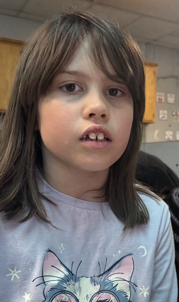 Willow sits in a classroom wearing a light-colored shirt with a cat design, looking toward the camera.