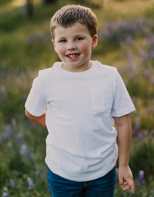 Tommy smiles while standing in a field of wildflowers, wearing a white t-shirt and jeans.